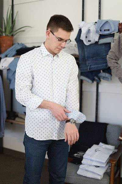 A man in a white shirt is standing in front of a stack of shirts.