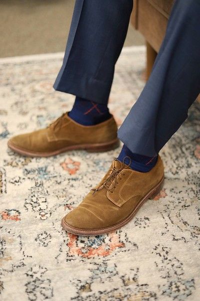 A man wearing blue socks and brown shoes is sitting on a rug.