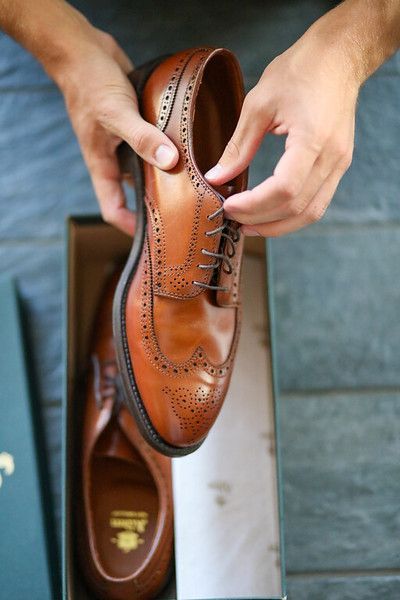 A person is tying a pair of brown shoes in a box