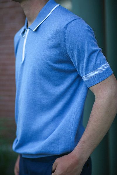 A man wearing a blue polo shirt is standing with his hands in his pockets.