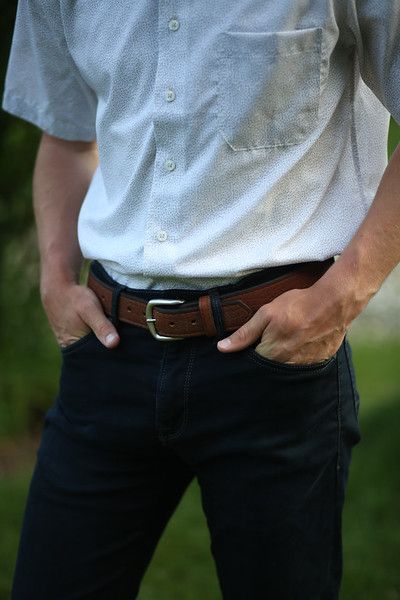 A man wearing a white shirt and a brown belt is standing with his hands in his pockets.