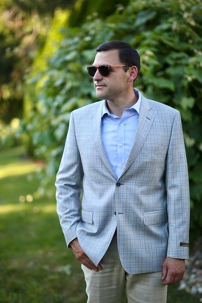 A man in a suit and sunglasses is standing in the grass.