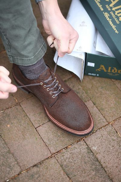A person is tying a pair of brown shoes on a brick sidewalk.