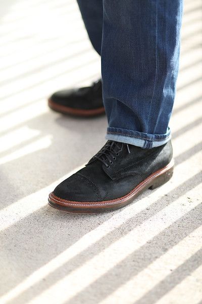 A person wearing jeans and black shoes is standing on a sidewalk.