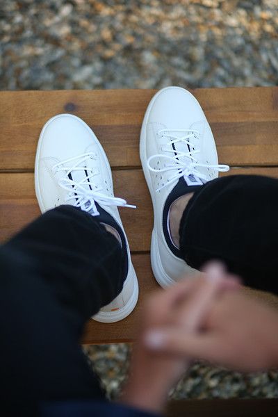 A person wearing white sneakers is sitting on a wooden bench.