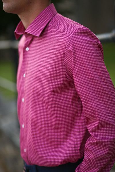 A man wearing a pink shirt is standing with his hands in his pockets.