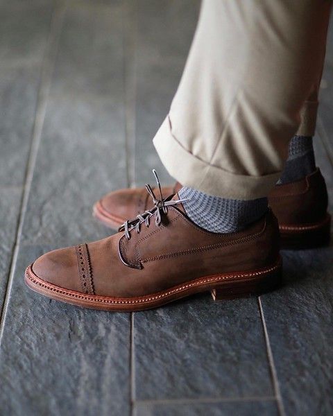 A person is wearing a pair of brown shoes with gray socks.