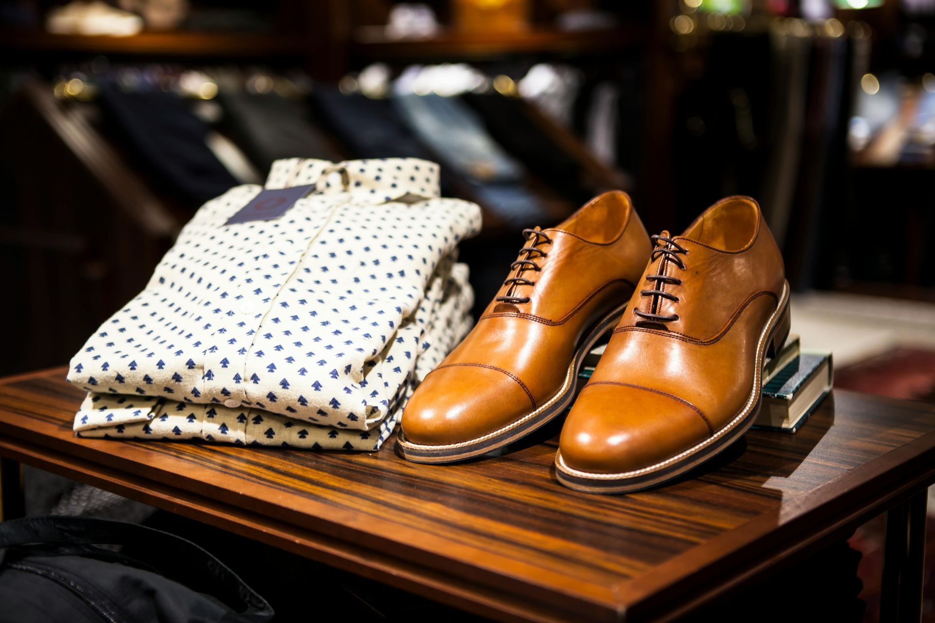 A pair of brown shoes sitting on top of a wooden table next to a stack of shirts.