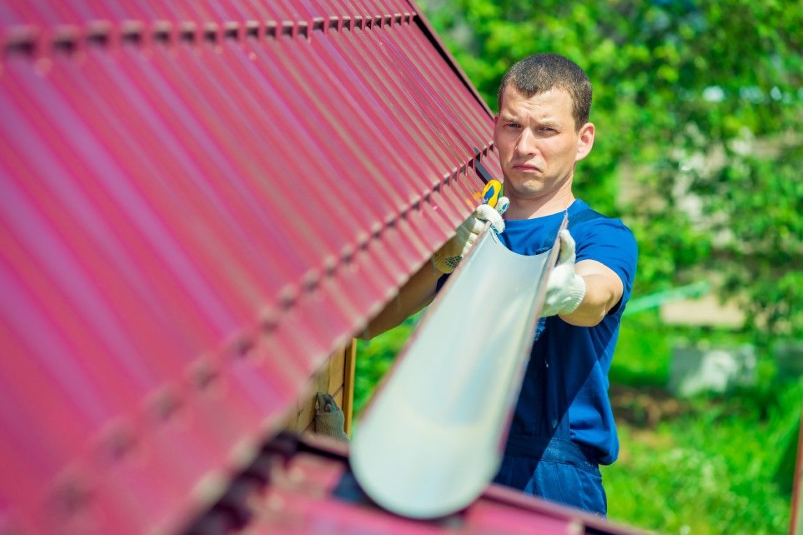 Technician in work gloves securing a gutter beneath a sloped red roof, preparing the drainage system for installation.