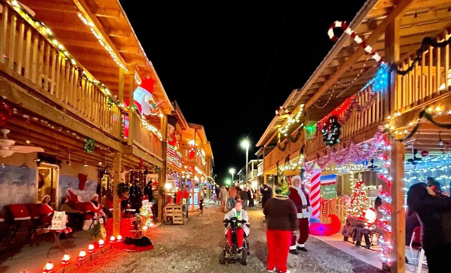 A group of people are walking down a walkway at Balls Creek Campground decorated with Christmas lights.