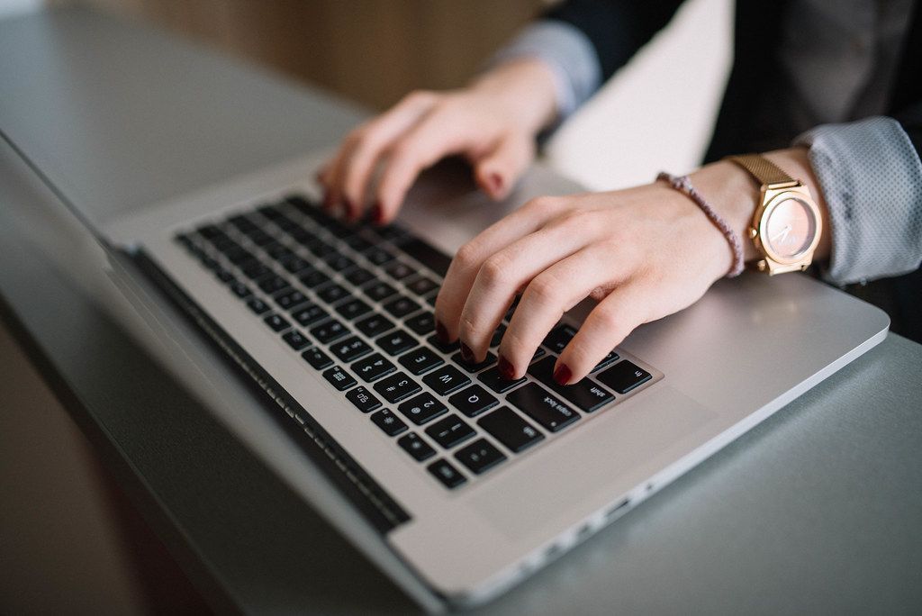 A woman wearing a watch is typing on a laptop