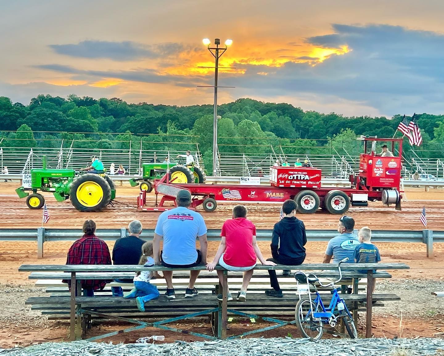 A group of people sitting on a bench watching a tractor pull