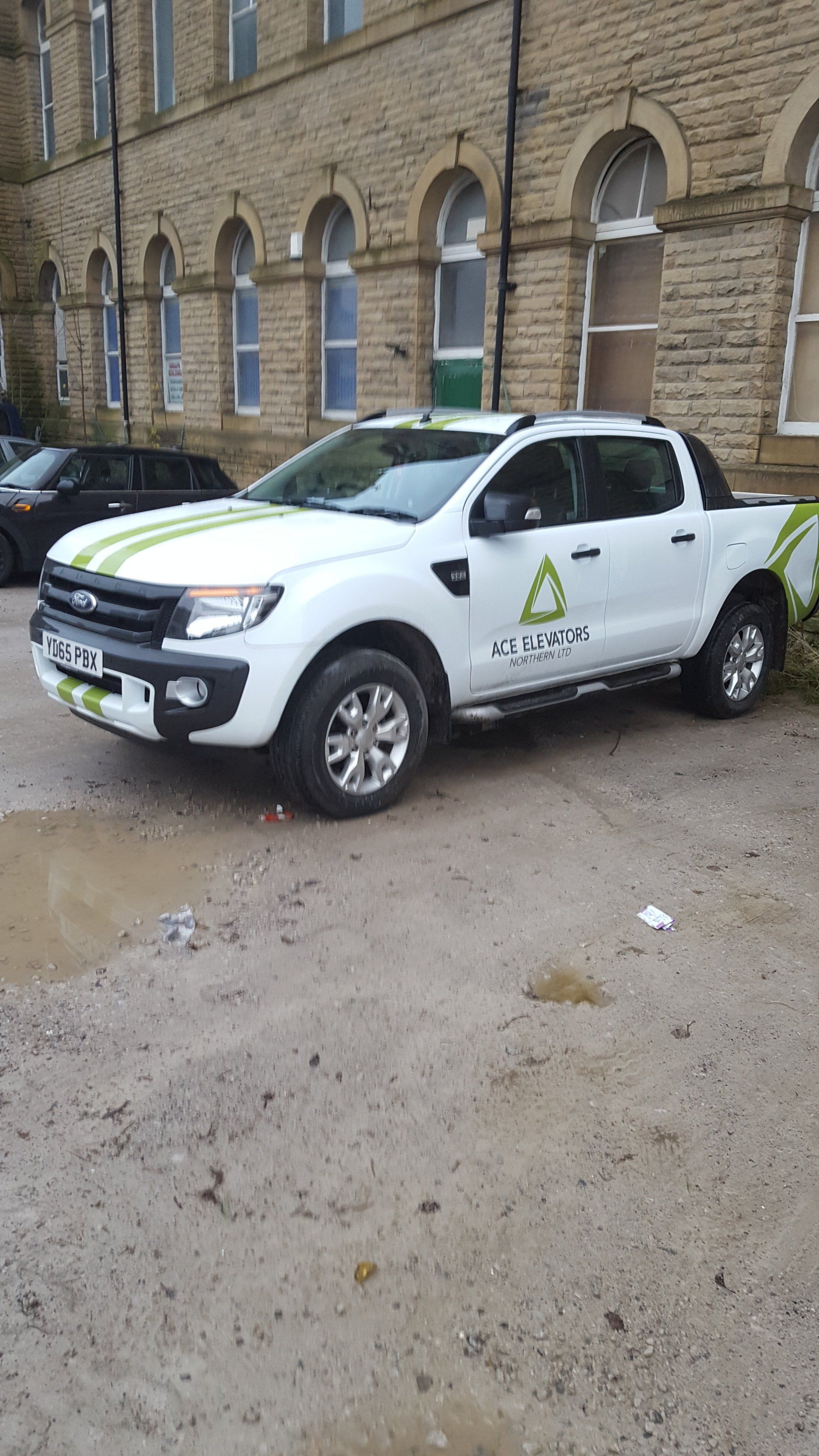White Ford Ranger pickup truck with green stripes, parked in front of a stone building.