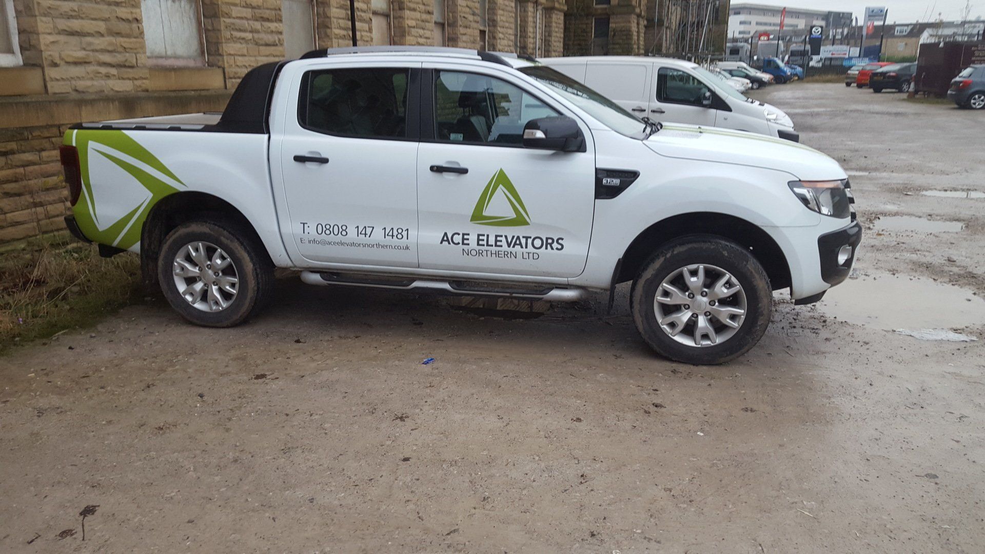 White pickup truck with green logo and lettering parked on a muddy lot.