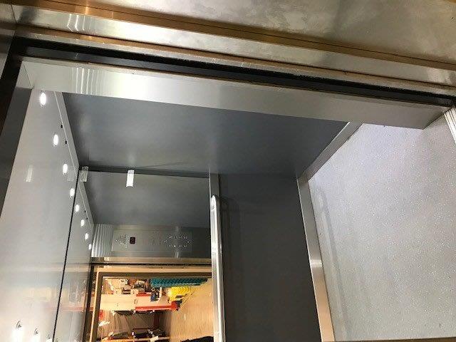 Interior of an elevator with stainless steel trim and gray walls. Doorway at top.