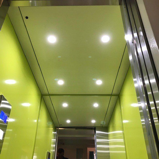 Interior of a lime green elevator with bright ceiling lights and steel accents. Doorway visible at the end.
