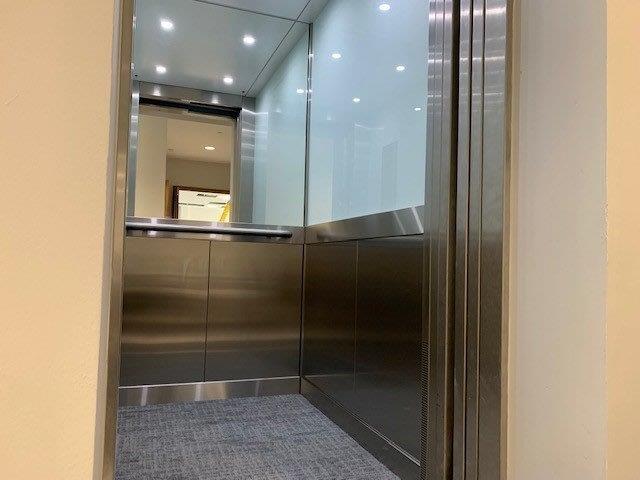 Stainless steel elevator interior with glass and carpet floor.