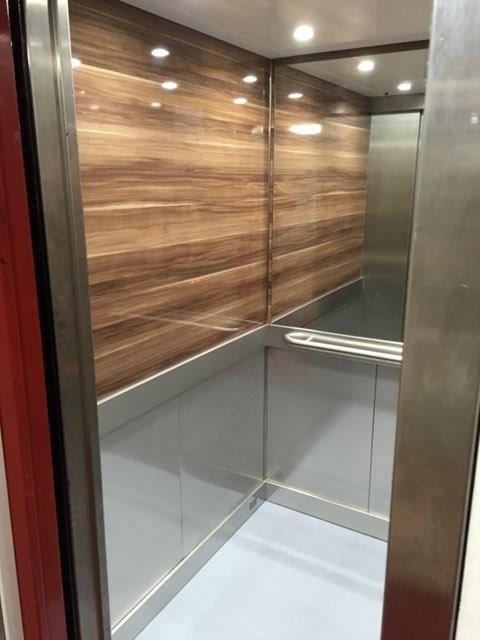 Empty elevator interior with wood paneling on one wall and stainless steel details.