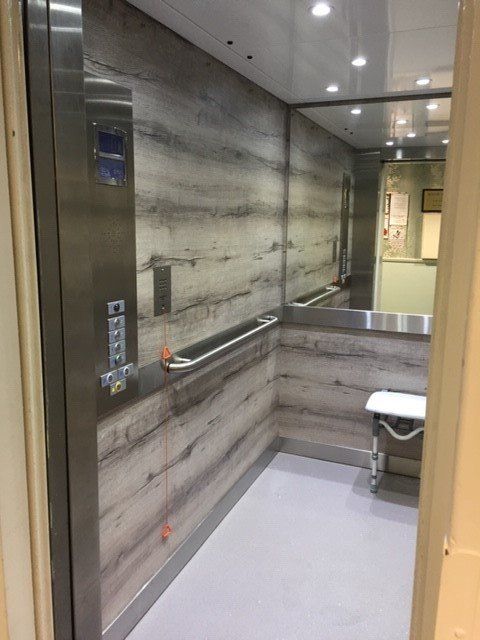 Elevator interior with wood-look walls, a stainless steel control panel, handrail, and a fold-down seat.