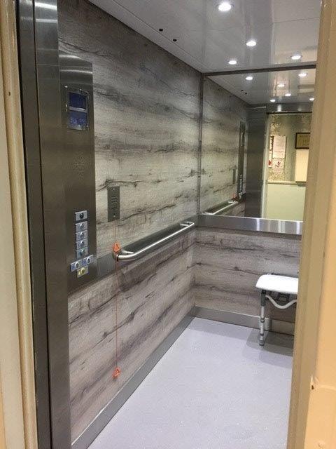 Elevator interior with wood-look paneling, a handrail, and a small fold-down seat.