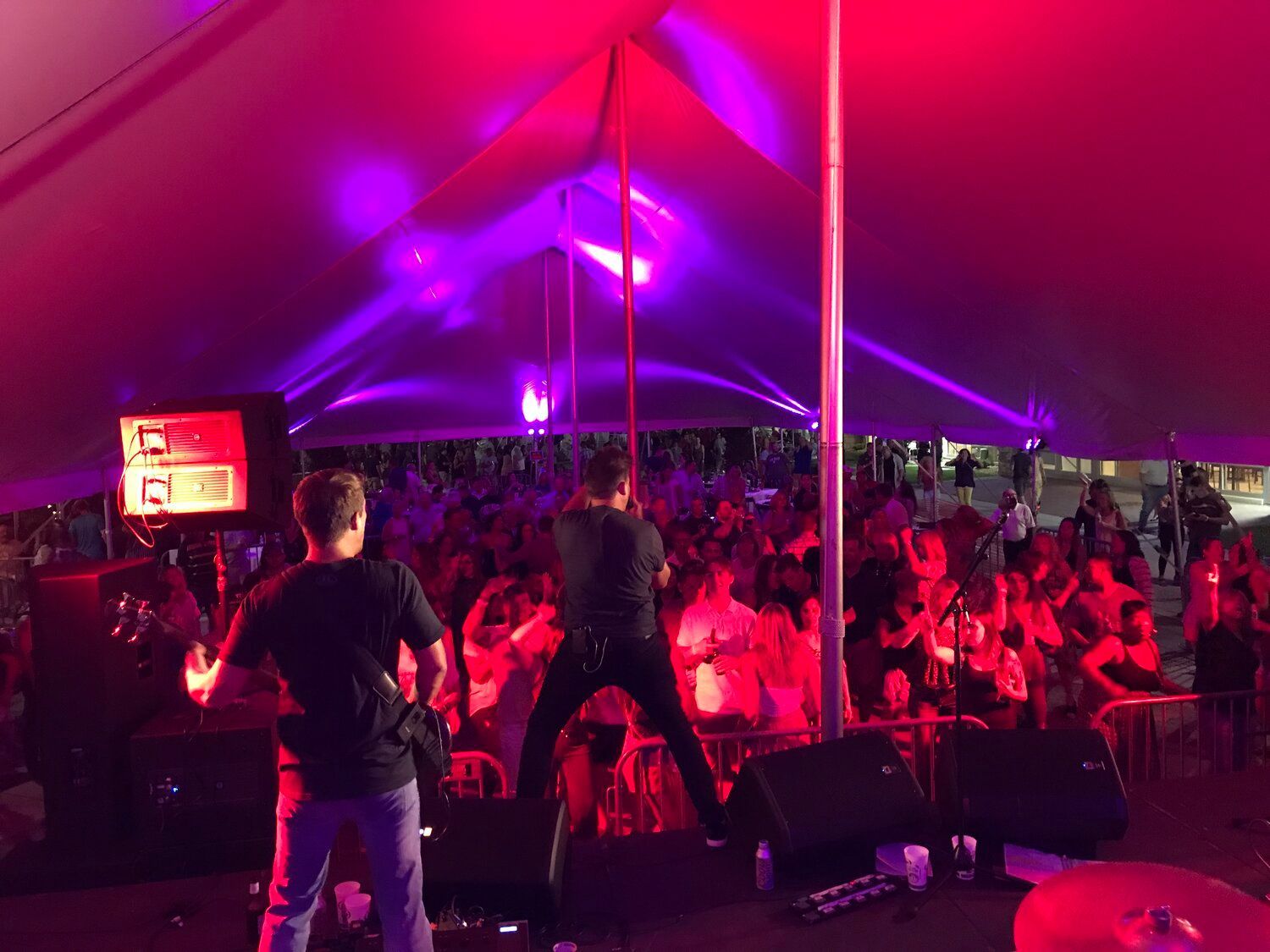 A band is playing under a tent with purple lights