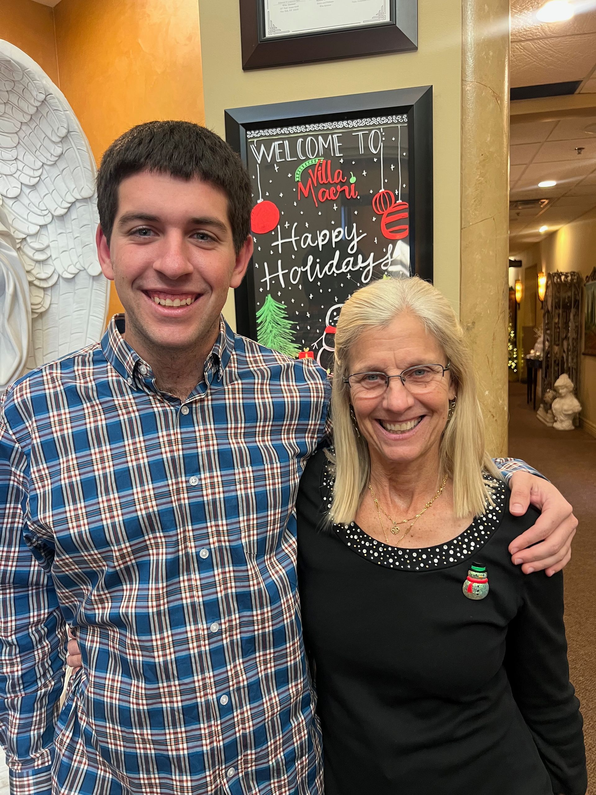 A man and woman are posing for a picture in front of a sign that says happy holiday