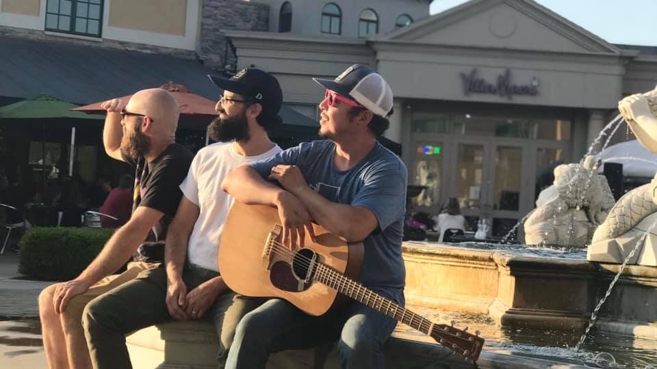 Three men are sitting on a fountain playing guitars.
