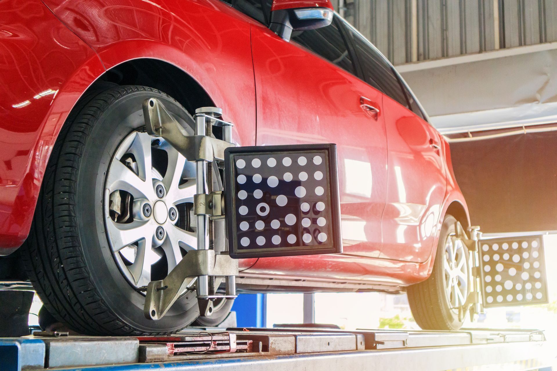 Red car undergoing wheel alignment at a mechanic shop, wheels attached to alignment equipment | PeePaw's Garage