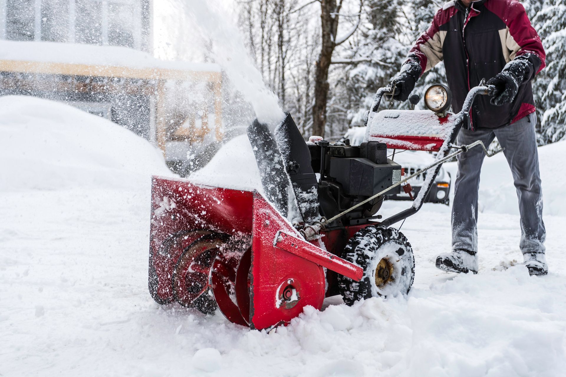 A man is using a snow blower to remove snow from a driveway.