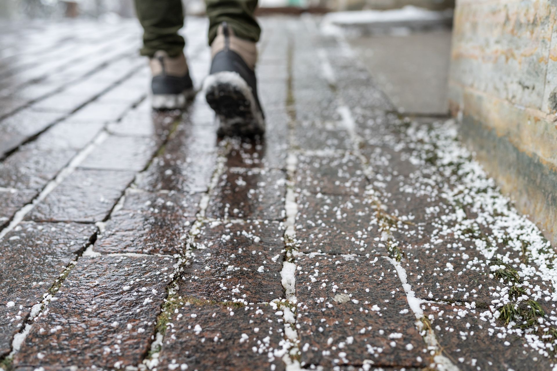 A person is walking on a brick sidewalk with snow on the ground.
