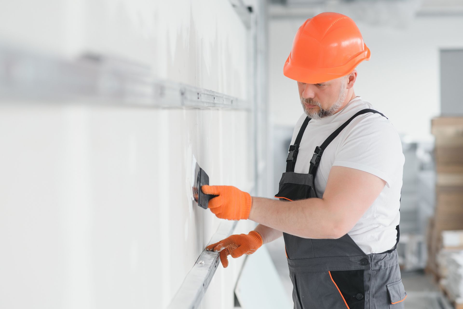 A man wearing a hard hat and orange gloves is working on a wall.