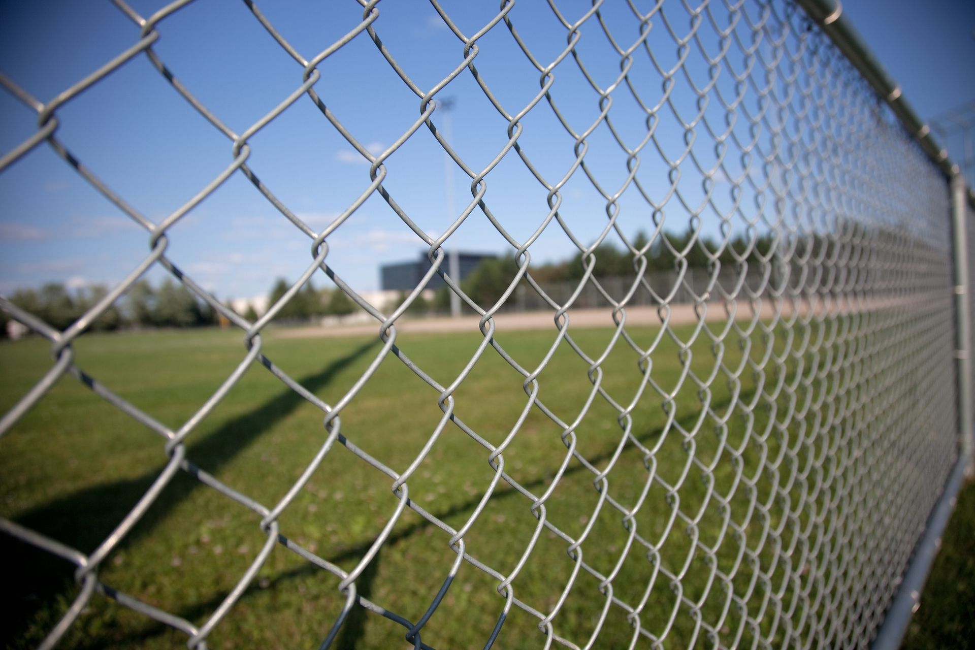 A chain link fence with a baseball field in the background