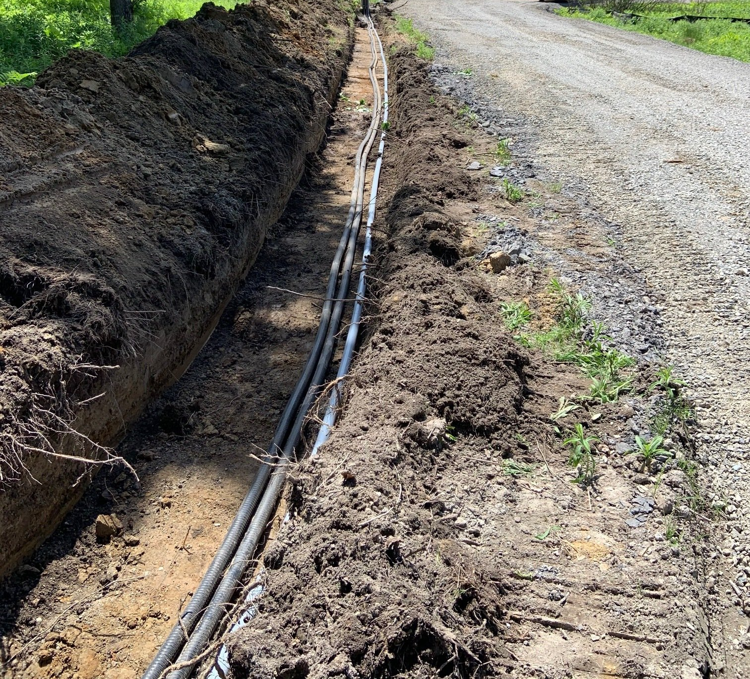 Un chemin de terre avec un tas de fils électriques posés dans la terre.