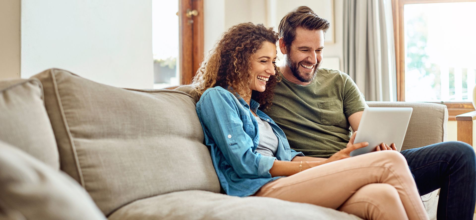 Un homme et une femme sont assis sur un canapé et regardent une tablette.