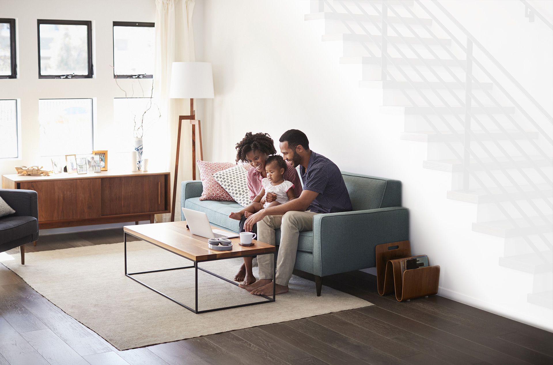 Une famille est assise sur un canapé dans un salon et regarde un ordinateur portable.