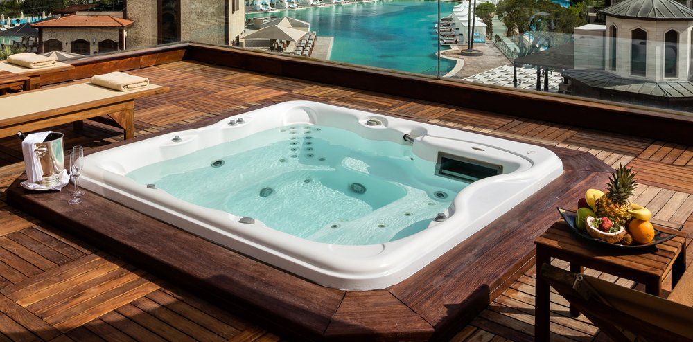 Un jacuzzi est installé sur une terrasse en bois à côté d'une piscine.