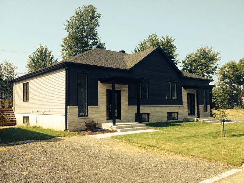 Une maison au toit noir est assise au sommet d'un champ vert luxuriant.