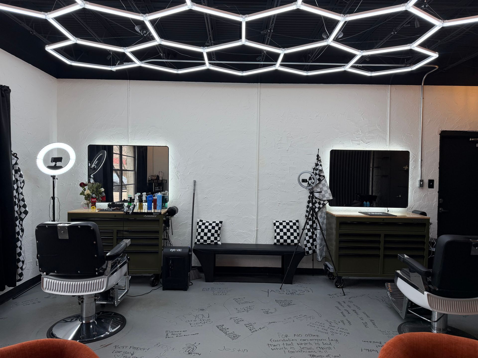 A modern barbershop with two workstations, black chairs, mirrors, and a hexagonal LED ceiling light grid.