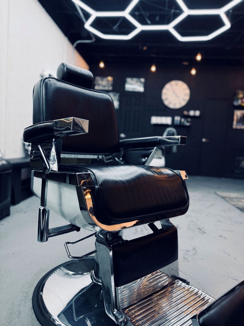 A vintage-style brown leather barber chair with white trim and chrome accents, positioned in a dimly lit setting.