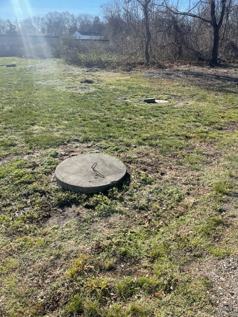 a concrete manhole cover is sitting in the middle of a grassy field .