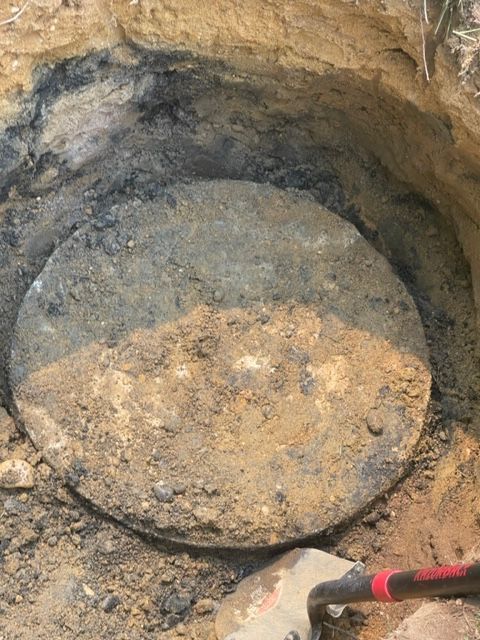 a manhole cover is sitting in the dirt next to a shovel