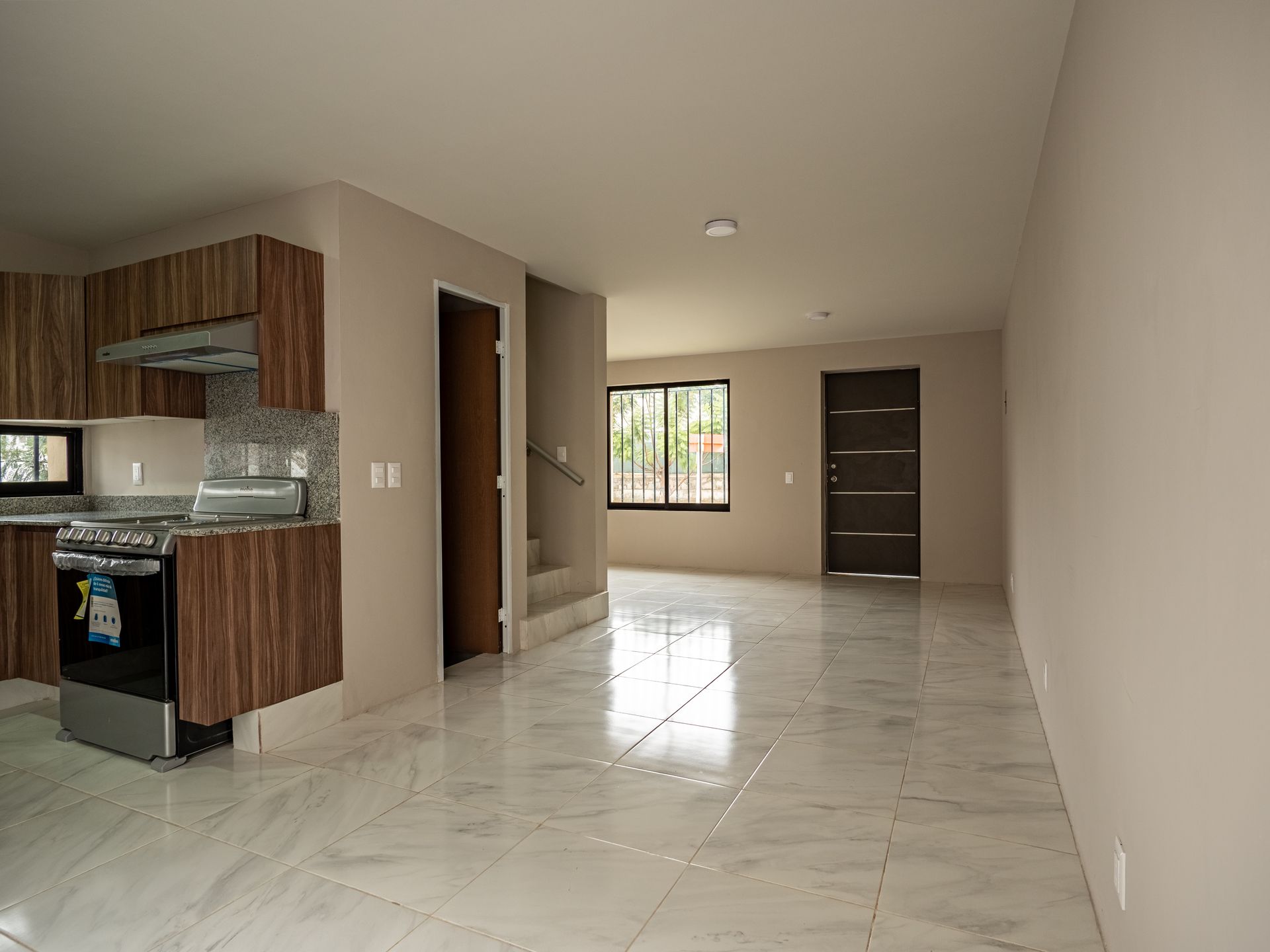 Una habitación vacía con una cocina y escaleras al fondo.