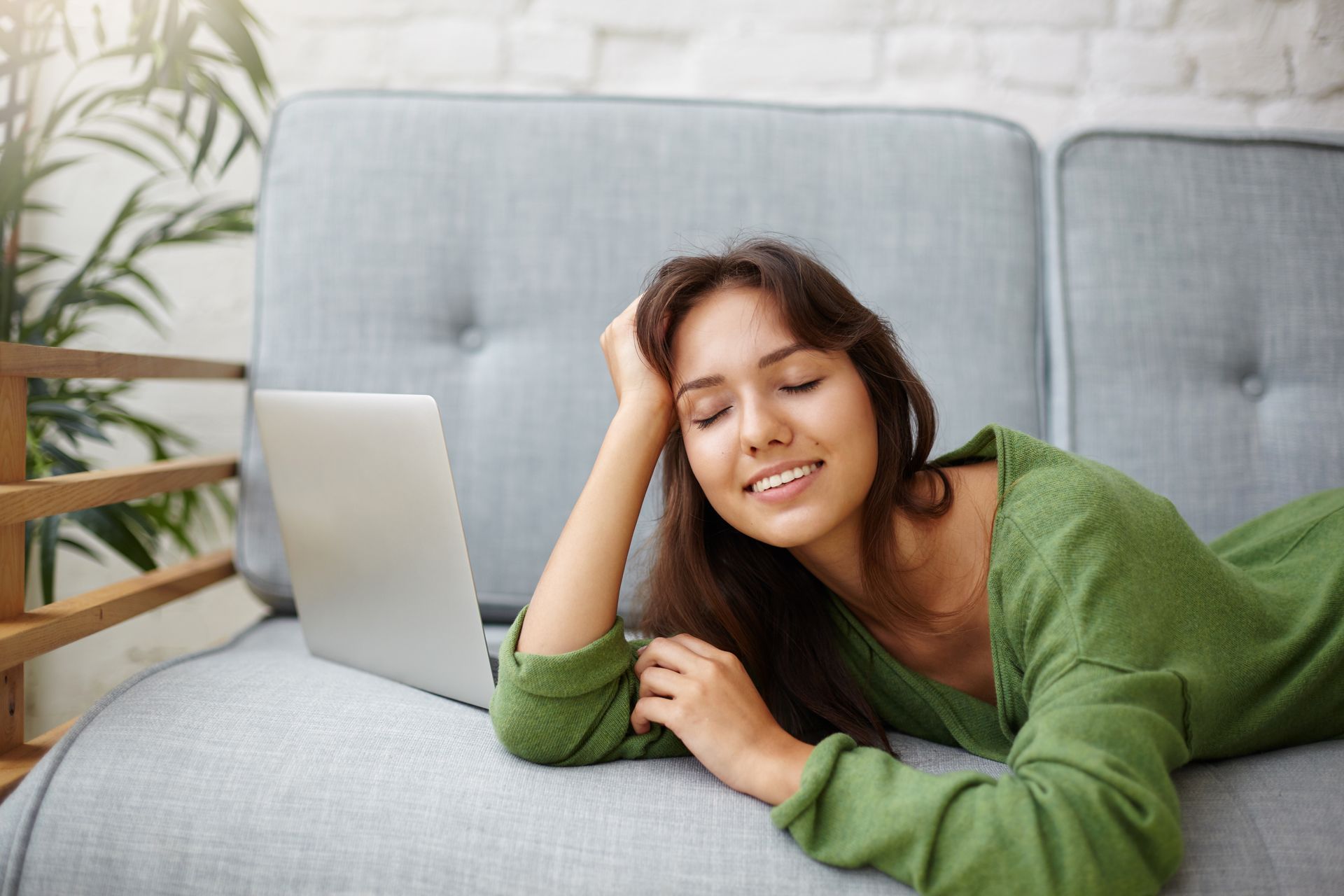 A woman is laying on a couch using a laptop computer.