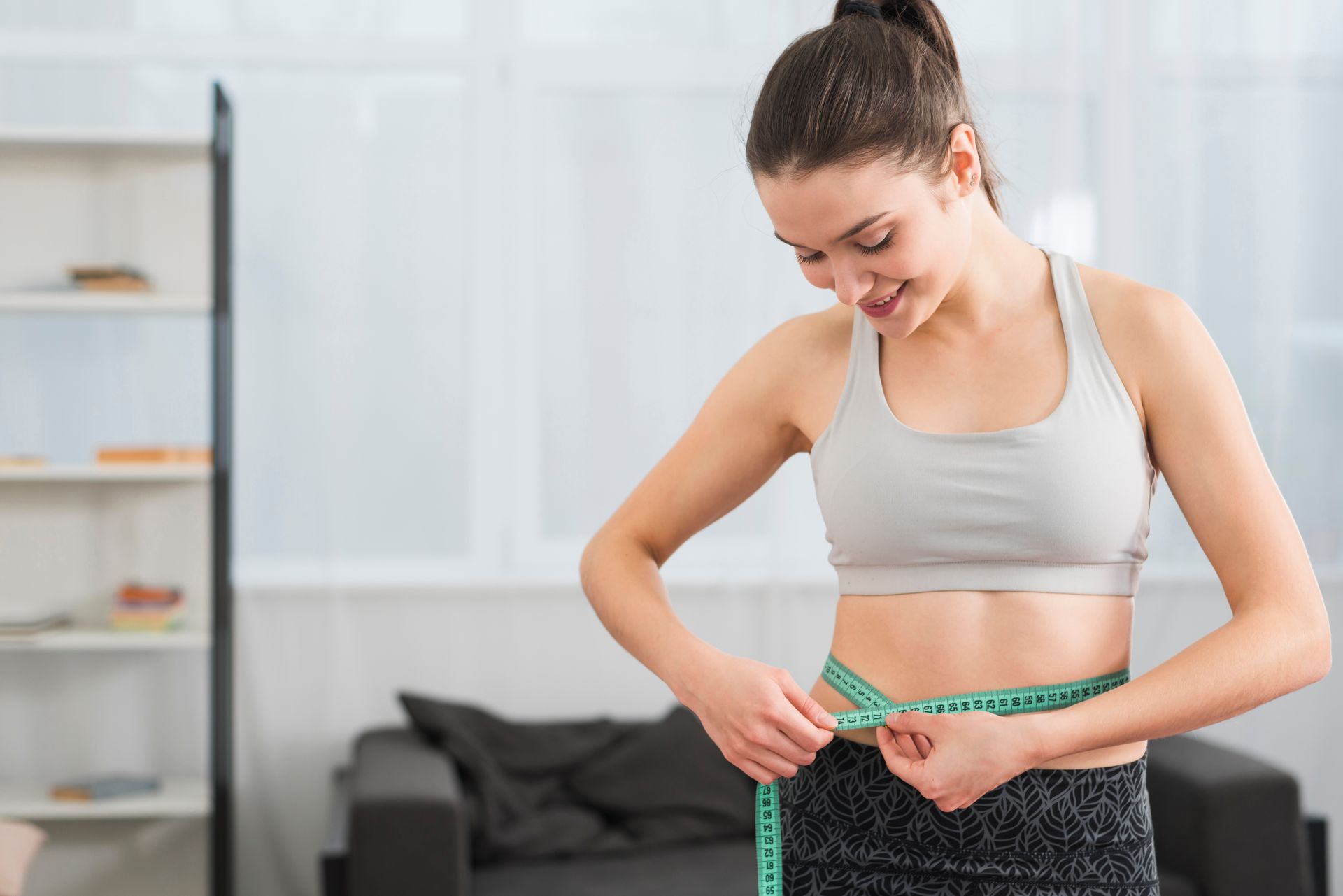 A woman is measuring her waist with a tape measure.