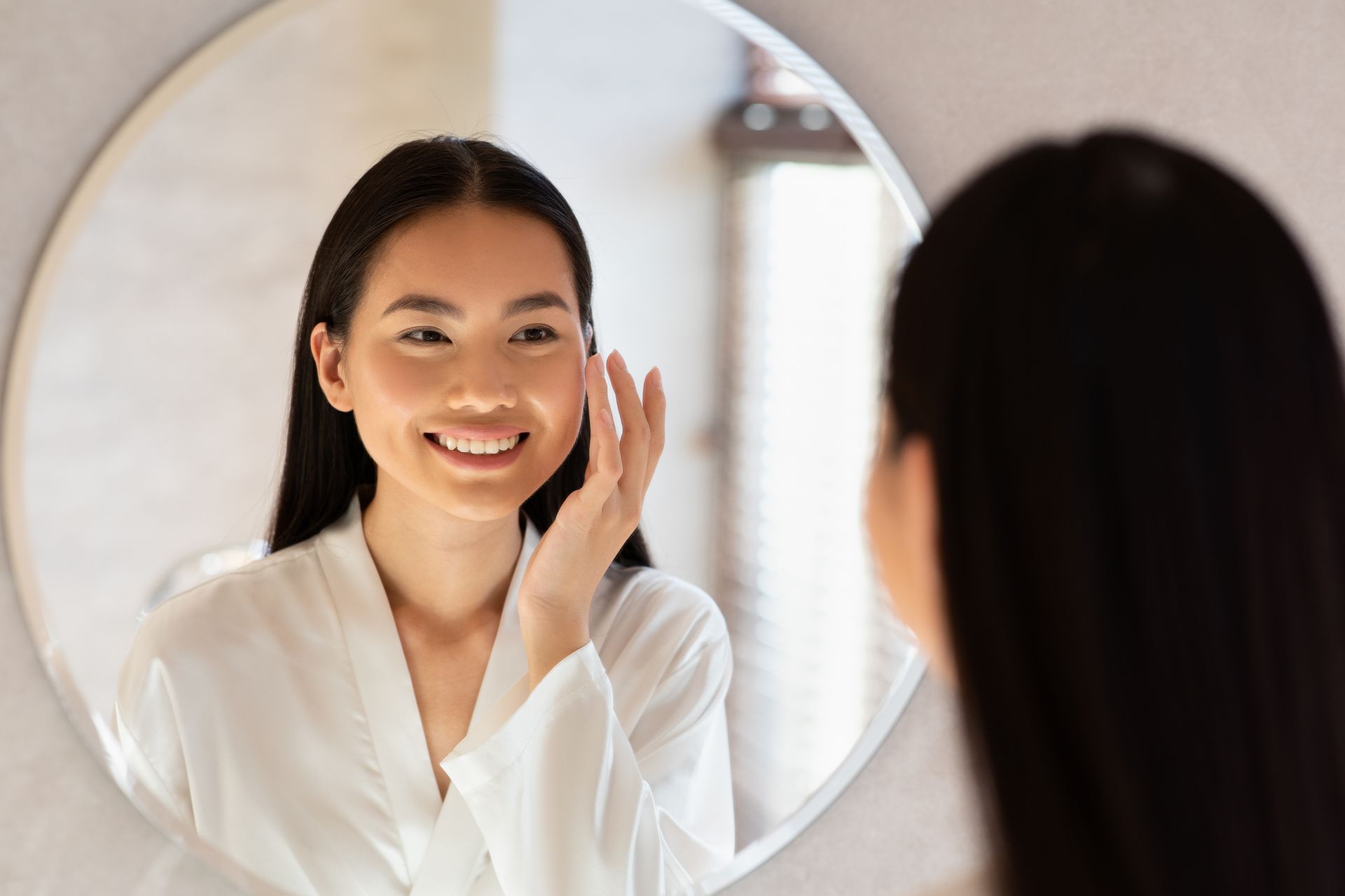 A woman is looking at her face in a mirror.