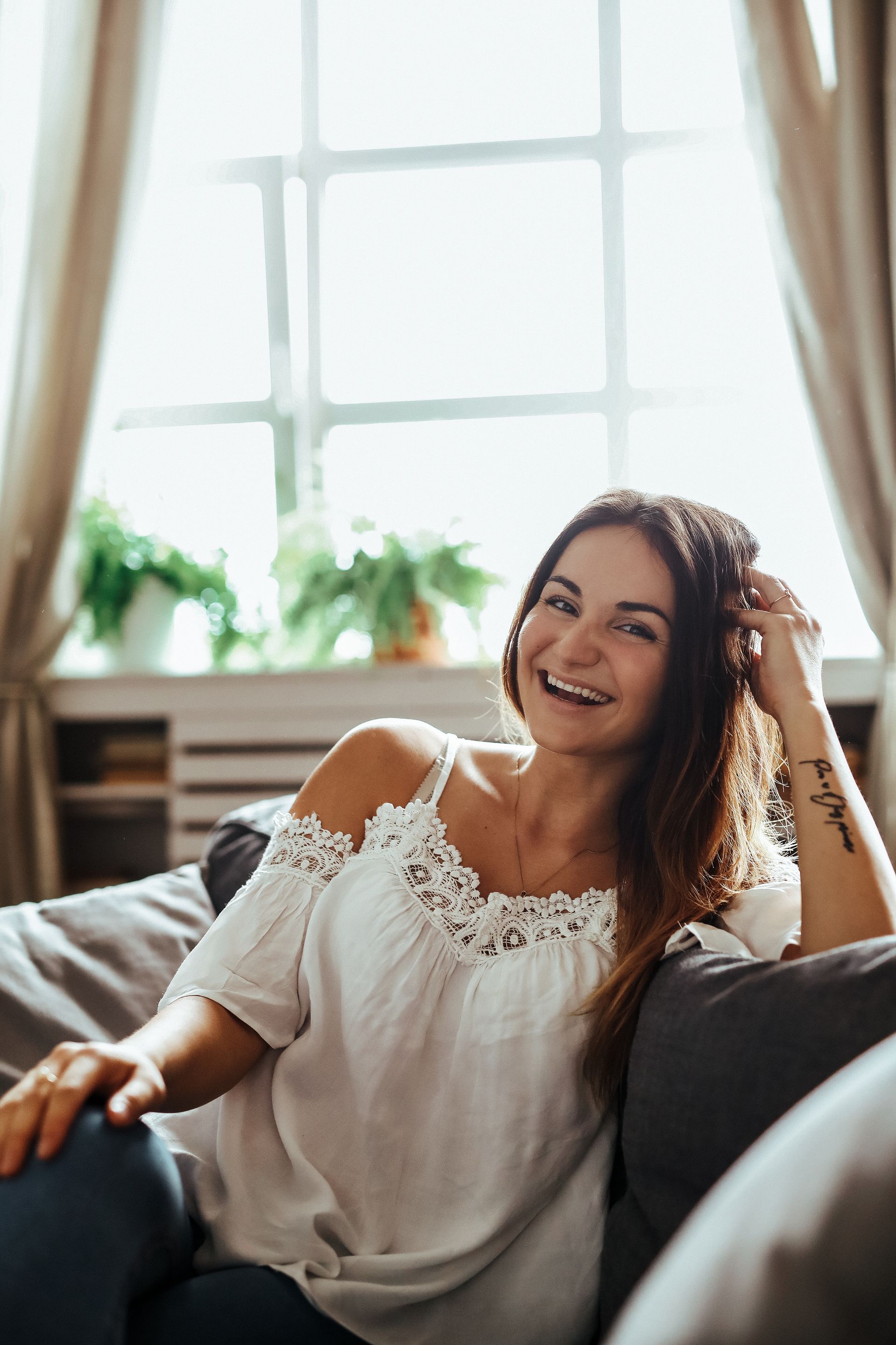 A woman is sitting on a couch in front of a window.