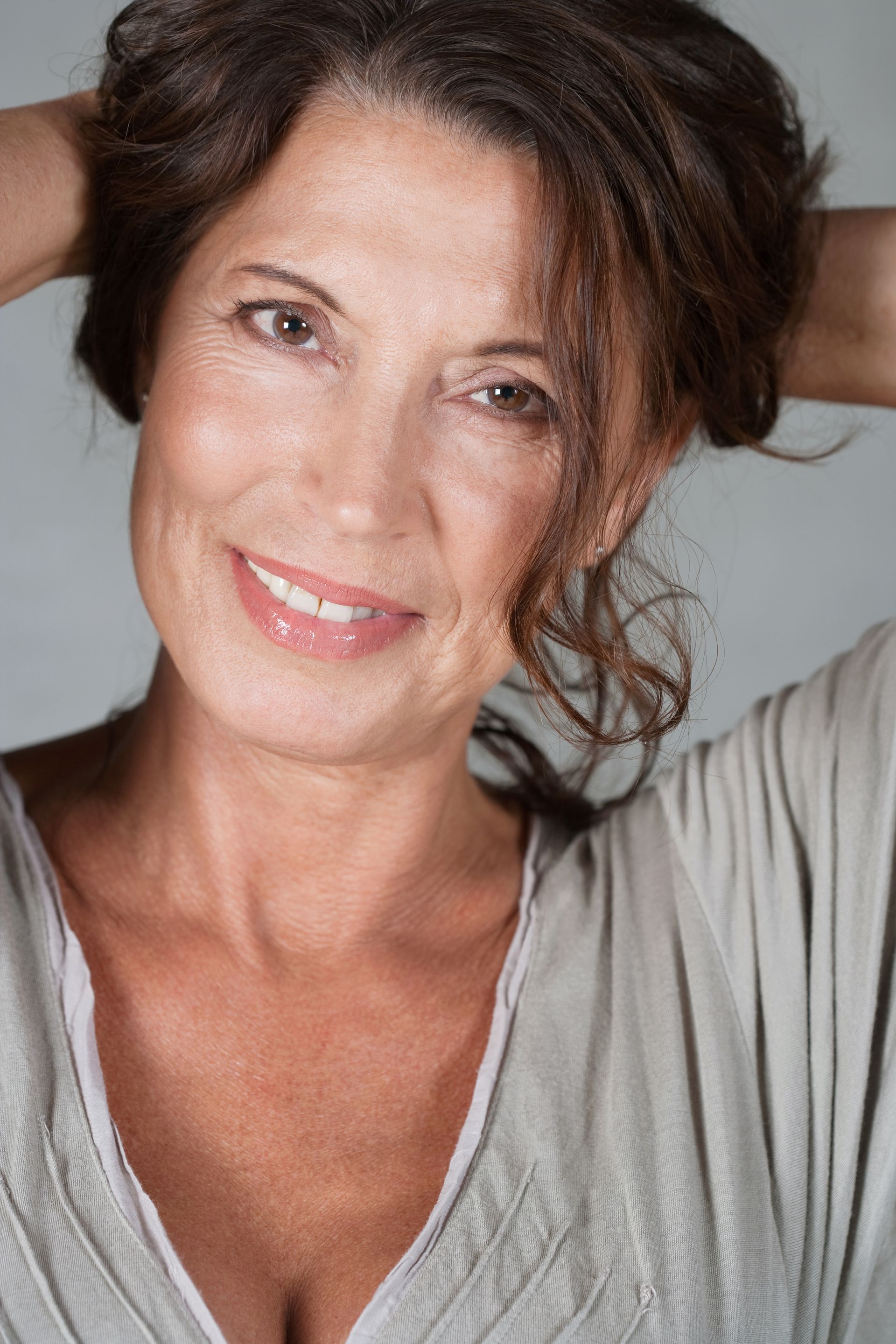 A woman is smiling with her hands in her hair.