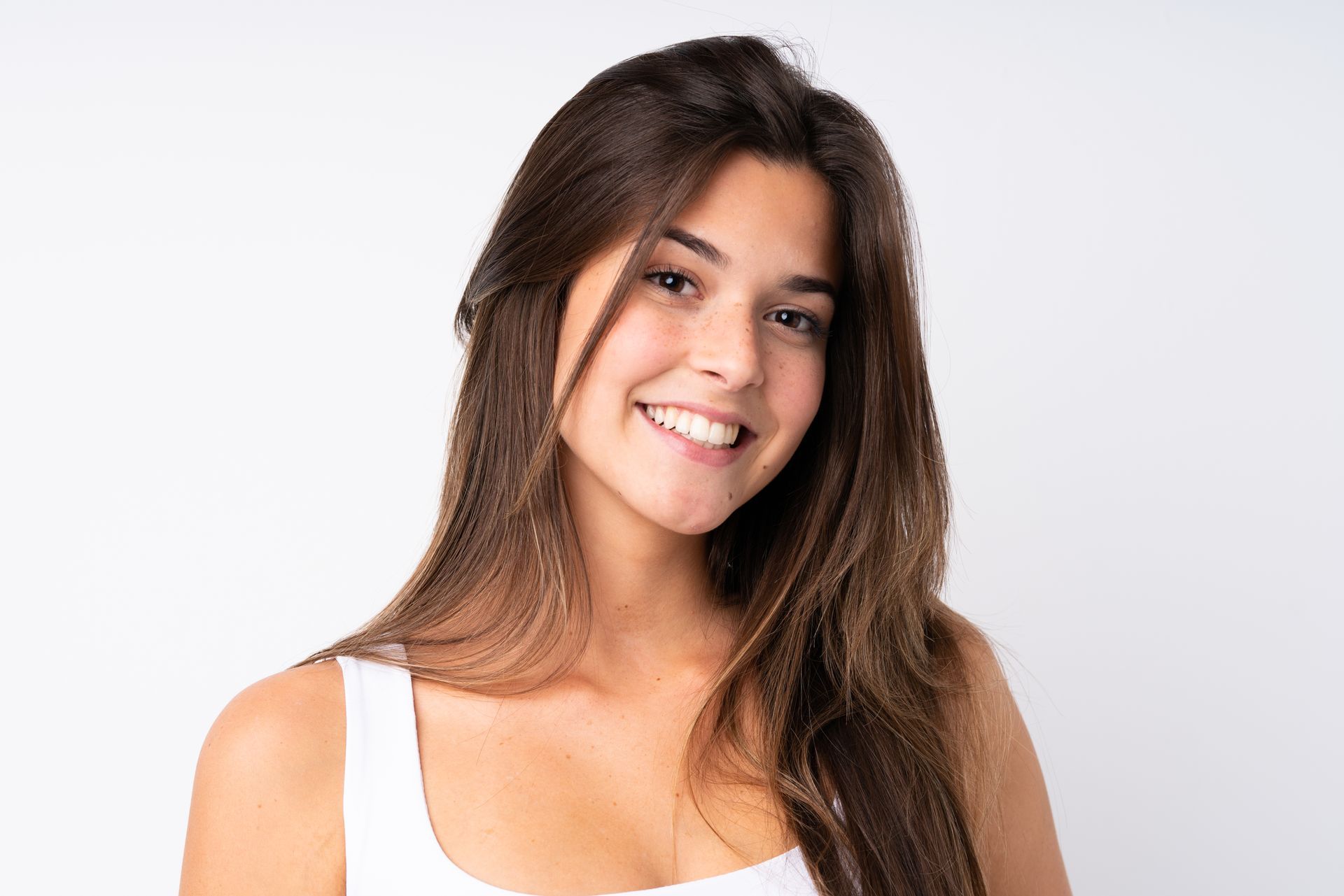 A woman with long hair is smiling and wearing a white tank top.