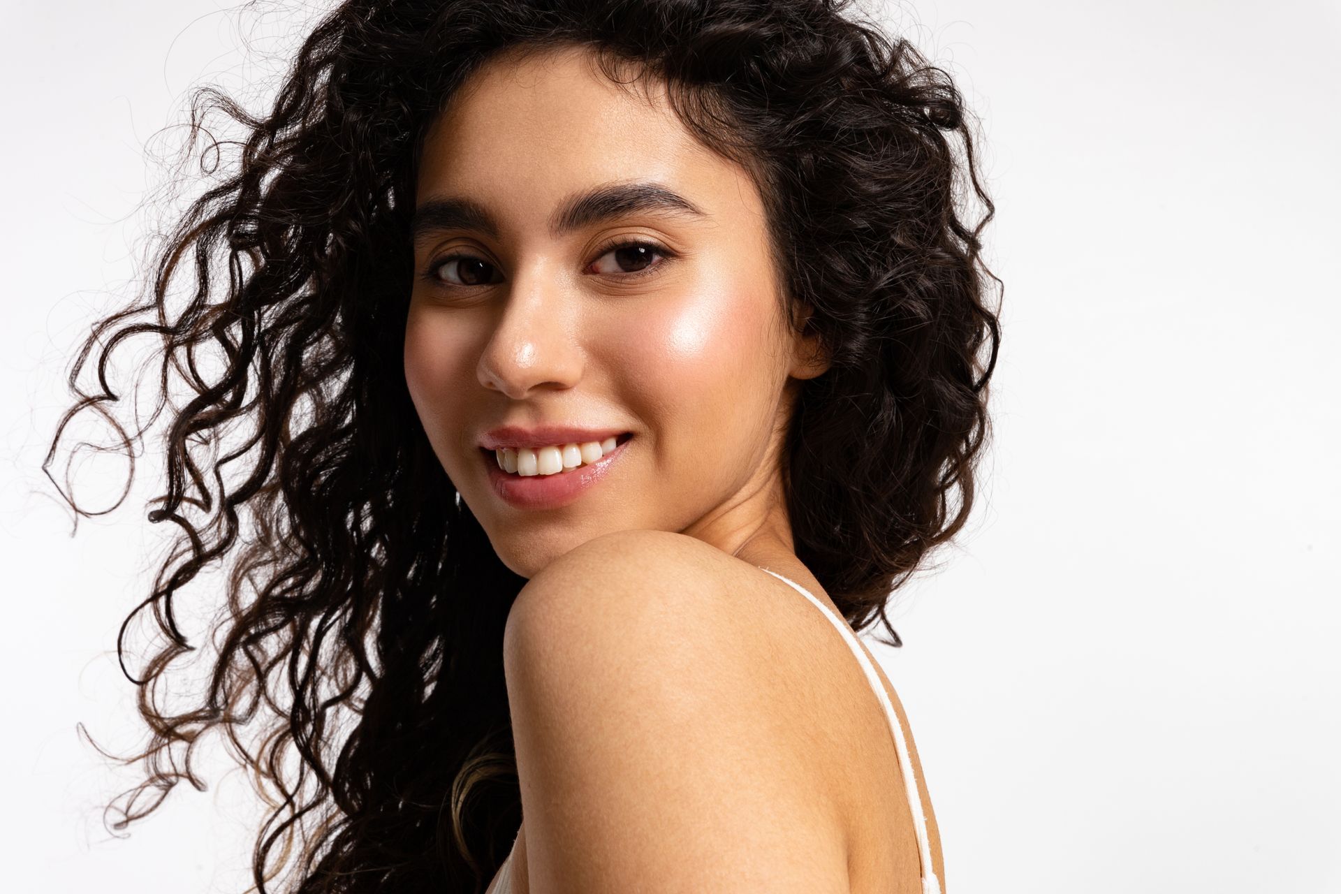 A woman with curly hair is smiling and looking over her shoulder.