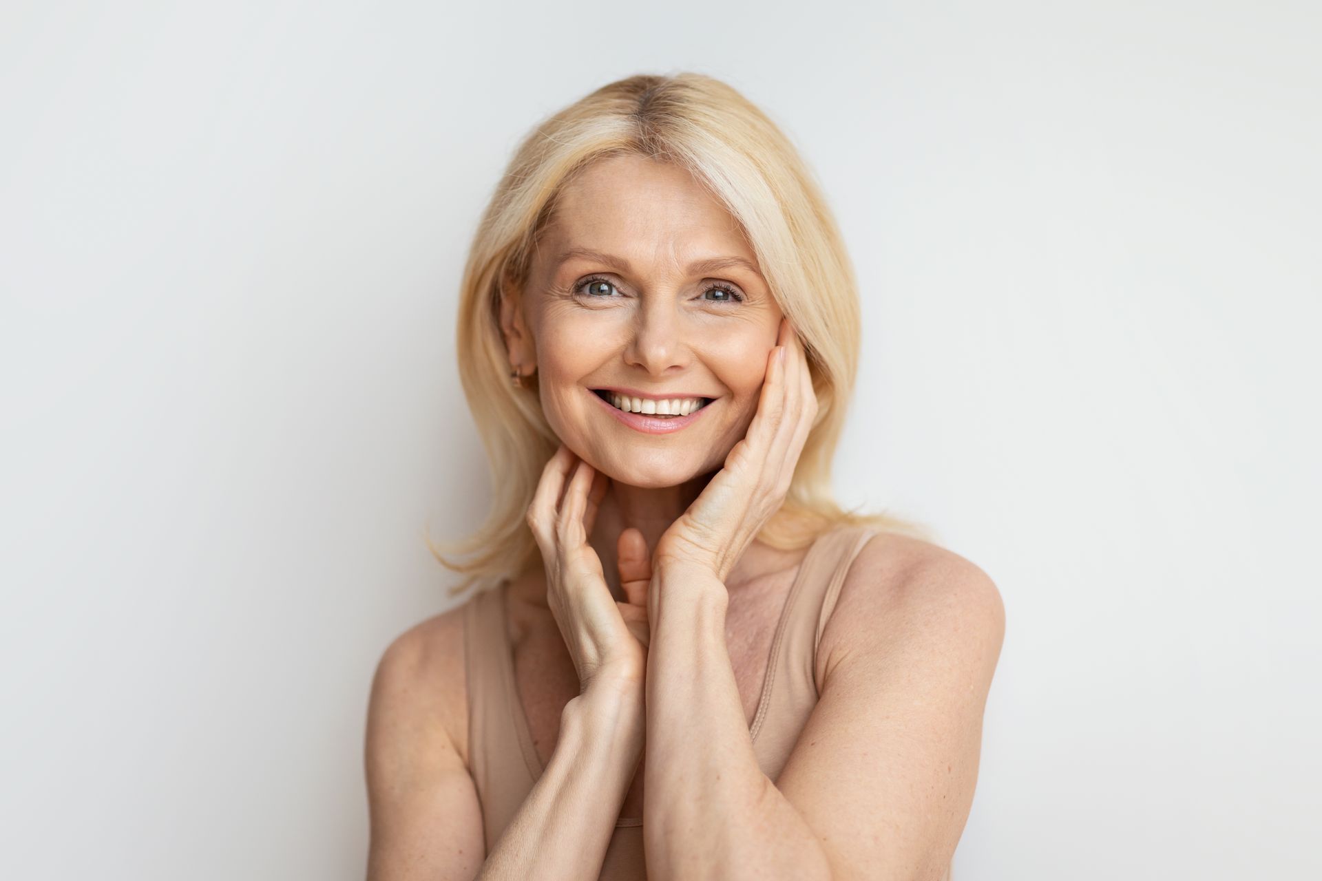 A woman is smiling and touching her face with her hands.